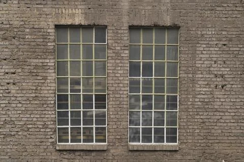 Two large industrial windows with small panes and metal frames are set in an old 스톡 사진