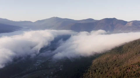 Two large moving clouds cover the mountain valley at dawn from aerial view. Stock Footage 144053130