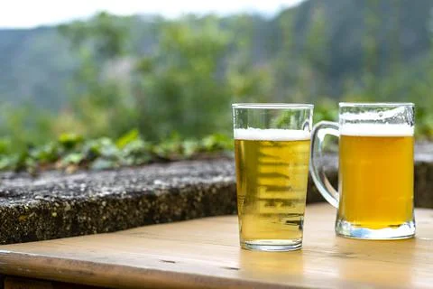 Two large mug of beer standing on a wooden table in the background a blurry r Stock Photos