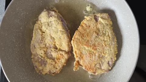 Two large pieces of battered meat are fried in boiling vegetable oil in a pan Stock Footage 244873825