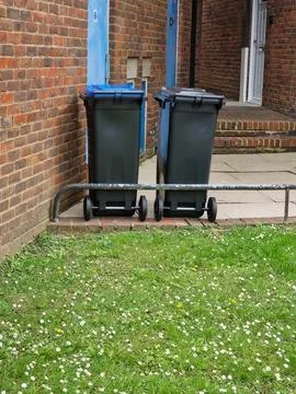 Two Large Plastic Wheelie Bins Parked Outside a Brick Residential Building Stock Photos