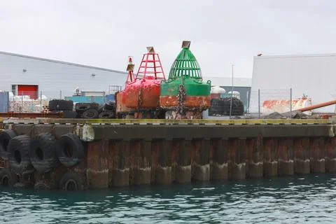 Two large red and green navigation buoys sit on a weathered industrial dock Stock Photos