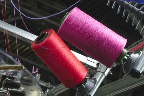 Two large spools of thread spin on machine frame. One spool is bright pink,   Stockfoto's