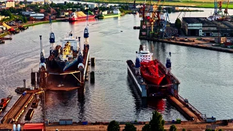 Two large vessels sit in floating dry docks along a busy industrial waterway Stock Footage 325570749