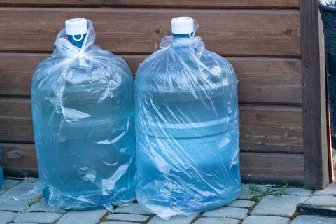 Two Large Water Bottles Wrapped in Plastic Bags Placed on a Stone Surface N.. Stock Photos
