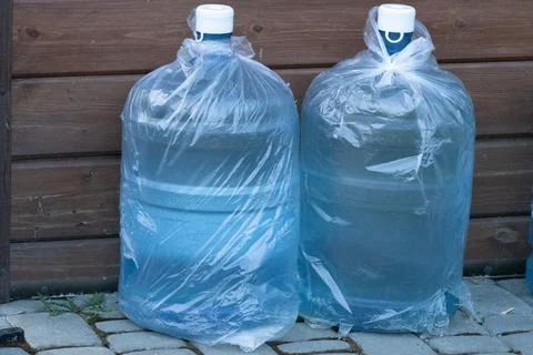 Two Large Water Bottles Wrapped in Clear Plastic Bags Placed on a Stone Pat.. Stock Photos