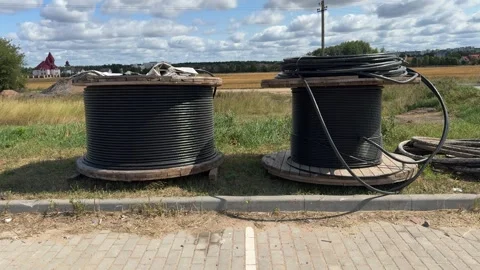 Two large wooden cable reels with black wire on grass near pavement Video stock 343409931