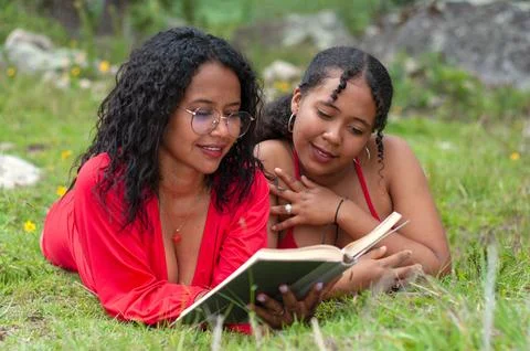 Two latina friends lying face down together reading a book attentively the girl Stock Photos