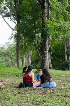 Two Latina mothers talking while children sit on grass during relaxed picni.. Stock Photos
