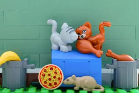 Two Lego cats and a mouse searching for food near trash cans. Fotos Stock