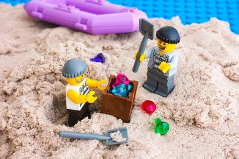 Two Lego robbers digging out box of gems from sand on the island Stock Photos