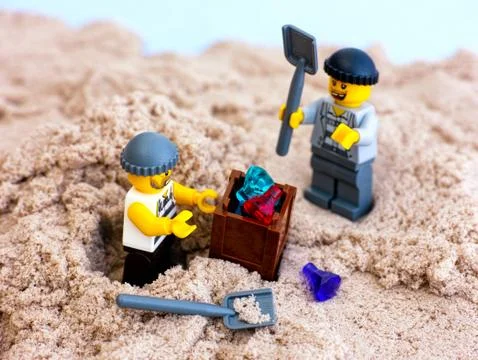Two Lego robbers digging out box with gems from sand Stock Photos