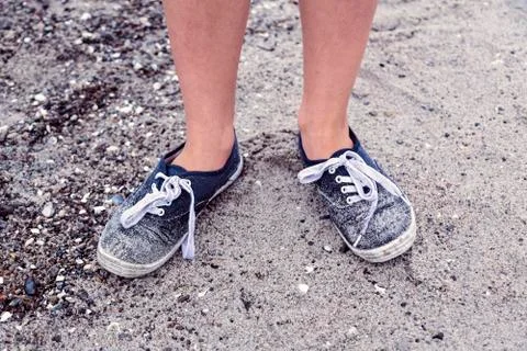 Two legs with old dirty blue shoes at the beach Stock Photos