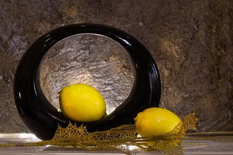 Two lemons and a black round vase with a golden branch with light. Brown ba.. Stock Photos