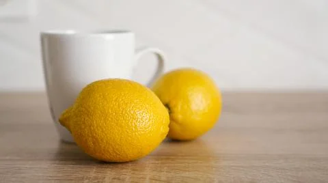 Two lemons on the kitchen table near a white mug of tea Stock Photos