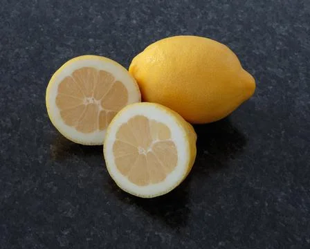 Two lemons (one cut) on a dark granite background Stock Photos