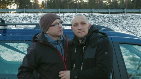Two LGBT guys, bald with a beard and wearing glasses and a hat hugging and Video stock 104898550