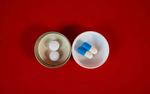 Two lids with tablets and blue capsule pair, top view on red Stock Photos