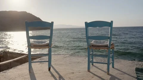 Two light blue chairs set in front of cliff and sea in afternoon sun in Greece Stock Footage 220526170
