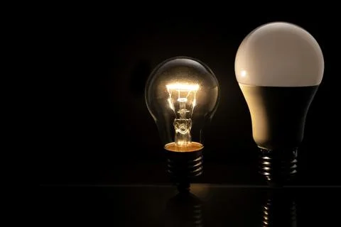 Two light bulbs on a black background, an incandescent light bulb is glowing and Stock Photos