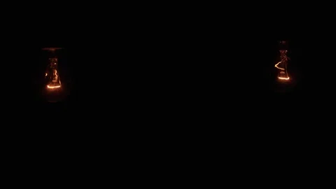 Two light bulbs hanging and swinging on a black background Stock Footage 263717717
