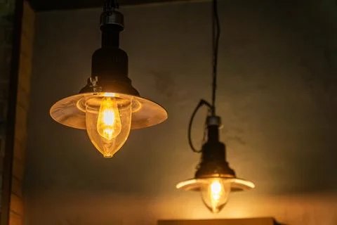 Two Light Bulbs Hanging From Ceiling, Representing Rising Electricity Costs and Stock Photos