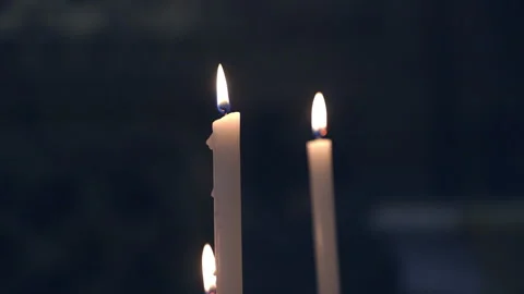 Two lit candles flicker gently in dark, quiet setting. Tall ivory tapers glow 库存影片 347296892