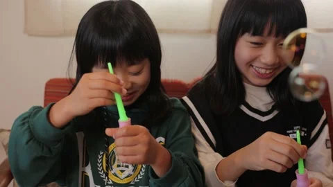 Two little asian sisters playing with soap bubble at home. Slow-mo. Stock Footage 228277983