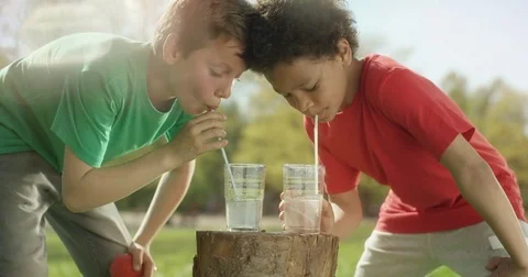 Two little boys are drinking water with a straw outside Stock Footage 77614469