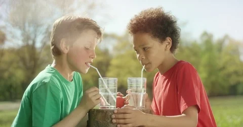 Two little boys are making bubbles with a straw outside Stock Footage 77614014