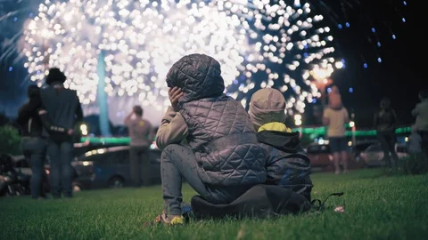 Two little children sit on the grass in the evening and watch fireworks. Salut Stock Footage 99578927