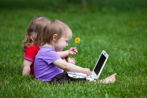 Two little children working together on the meadow with a laptop. Stock Photos