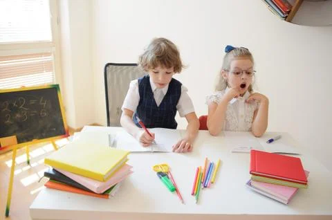 Two little classmate, boy and girl, are sitting at the same desk. Stock Photos