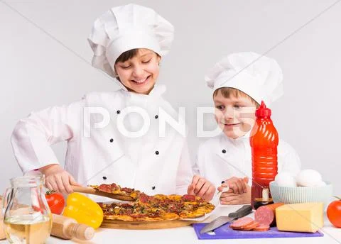 Two little cooks portioning cooked pizza Stock Photos