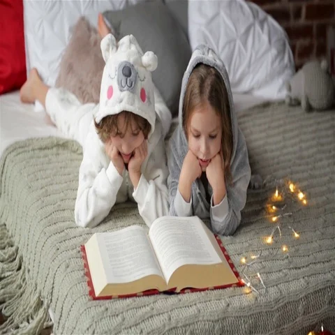 Two little cute siblings reading a book in bed near Christmas tree with lights a Stock Footage 69361228