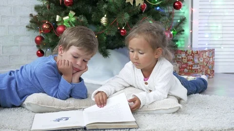 Two little cute siblings reading a book on the floor near Christmas tree Stock Footage 76986930