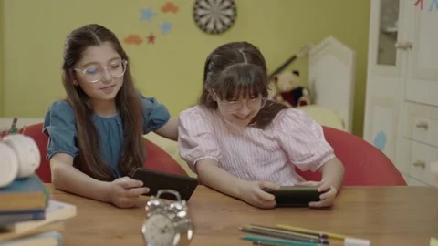 Two little girl friends playing online games with smartphones at home daycare. Stock Footage 203747553