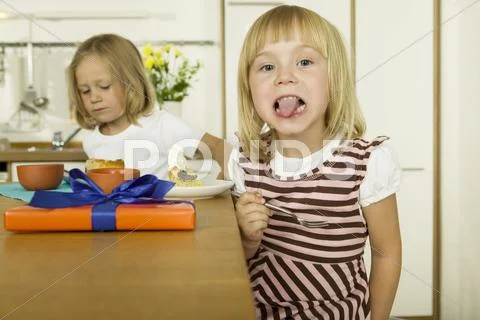 Two little girls (4-5) eating cake in kitchen Stock Photos