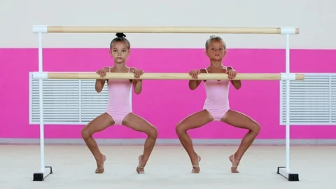 Two little girls gymnasts warming up in the studio - squatting standing on their Vidéo 162461208