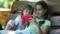 Two little girls with red smartphone sits on the swing bench HD Footage