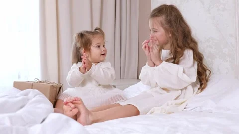 Two little girls sit on a bed in the morning, joyfully clapping their hands Stock Footage 314063013