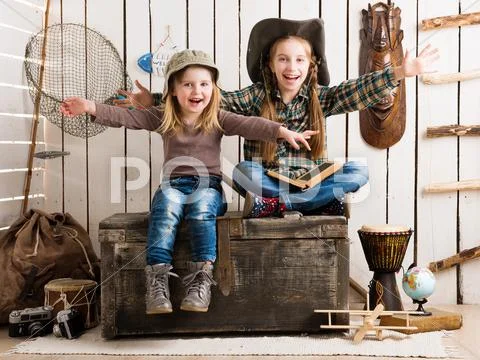 Two little girls sitting on wooden chest with hands up Stock Photos