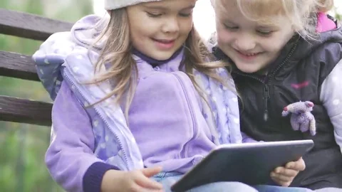 Two little girls with tablet computer sits on the bench in garden Stock Footage 69245043