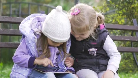 Two little girls with tablet computer sits on the bench in garden Stock Footage 69245705