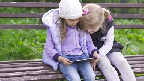 Two little girls with tablet computer sits on the bench in garden Stock Footage 69245877