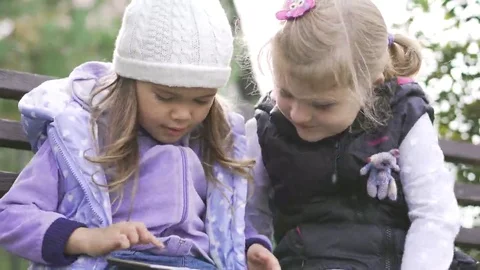 Two little girls with tablet computer sits on the bench in garden Vídeo Stock 69247092