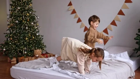 Two little sibling children having fun at home, jumping on a bed on Christmas Stock Footage 314066010