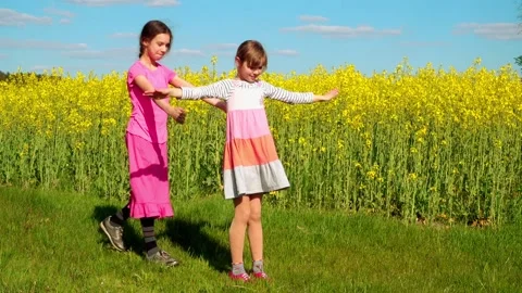 Two little sisters are playing against the backdrop of a large rapeseed field Stock Footage 114515990