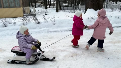 Two little sisters carrying a third sister by a rope who is sitting on a sled 库存影片 264115069