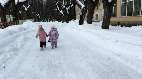 Two little sisters carrying a third sister by a rope who is sitting on a sled 库存影片 264115084